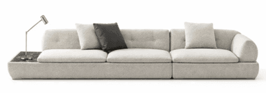 A long, contemporary modular sofa upholstered in a light, textured fabric, likely bouclé. It features multiple seat and back cushions, some with button tufting. An integrated dark, veined marble side table is positioned at one end, supporting a small, silver-toned task lamp. The sofa has a low-profile design with soft, rounded edges. — 3D model