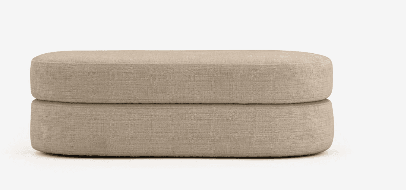 An upholstered two-tier ottoman in a light beige textured fabric, featuring a soft, rounded capsule shape. — 3D model