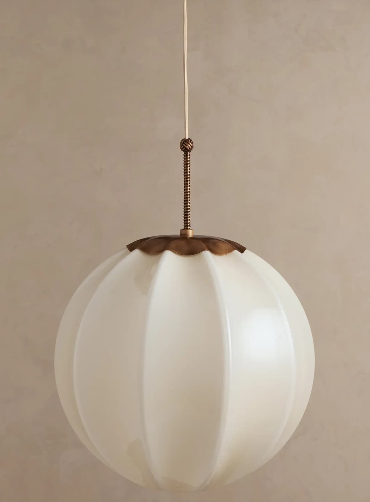 A single pendant light featuring a spherical, fluted opal glass shade suspended from a white cord with brass-toned metal fittings. — 3D model