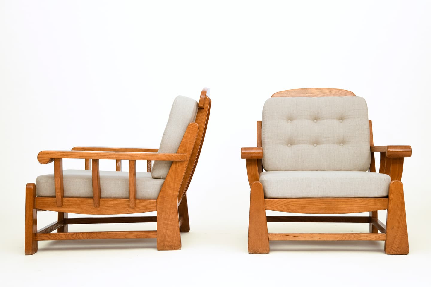 A pair of lounge chairs, each featuring a robust wooden frame with light-colored upholstered seat and back cushions. The back cushions are tufted with six buttons. The chairs display a sturdy, classic design with prominent wooden armrests and base structure. — 3D model