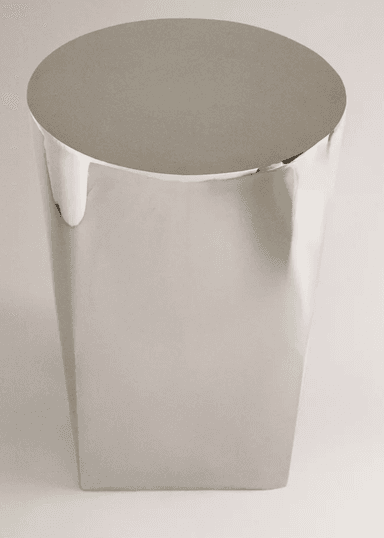 A sleek, cylindrical pedestal table featuring a polished metallic finish. The object has a uniform diameter from top to bottom, with a perfectly flat top surface. The highly reflective surface suggests a metallic material such as stainless steel or chrome, giving it a modern and minimalist aesthetic. — 3D model