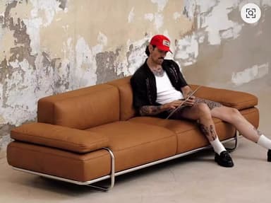 A modern sofa with clean lines, featuring cognac leather upholstery and a polished metal frame that forms the base and track arms. It includes two seat cushions, two back cushions, and two matching lumbar pillows. — 3D model