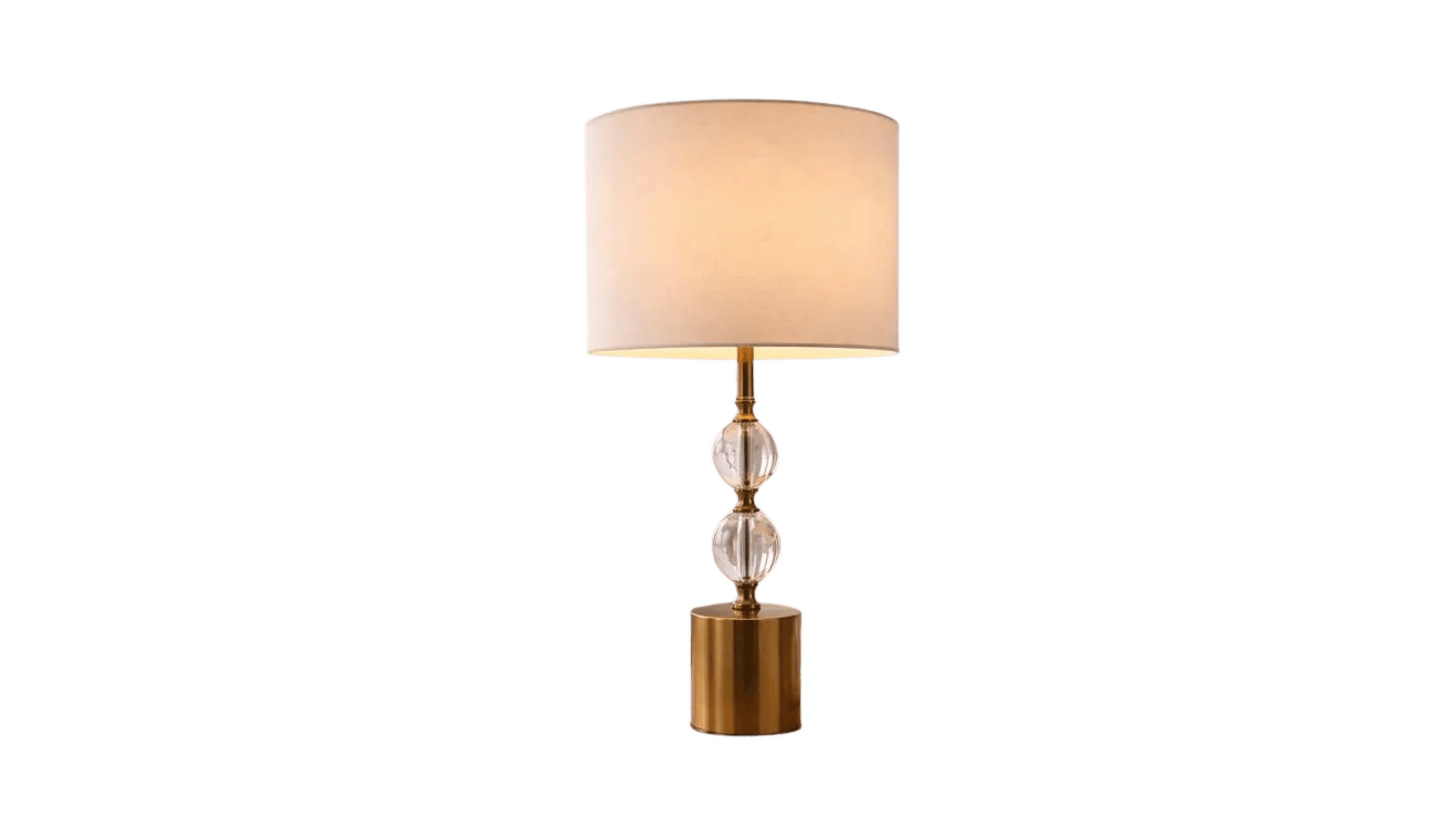 A table lamp with a cylindrical, brushed gold-colored base. The stem supporting the shade features two clear, faceted crystal spheres stacked vertically. The lampshade is cylindrical and made of a light-colored fabric, emitting a warm glow. — 3D model