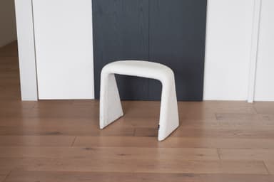 A white, textured stool with a unique U-shaped base. The stool appears to be upholstered in a boucle or teddy bear fabric. Its curved structure provides a modern and organic aesthetic. — 3D model