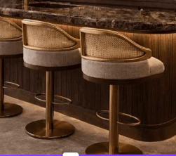 A sophisticated swivel bar stool featuring a brass-finished metal frame and disc base, a woven cane backrest, and an upholstered seat in a light, neutral fabric. It is height-adjustable with a hydraulic lift mechanism and includes a circular footrest. — 3D model