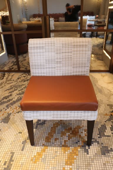 An armless dining chair featuring a light, patterned fabric upholstered back and frame, contrasted with a smooth, warm brown leather seat cushion. The chair stands on four dark, slightly tapered wooden legs. — 3D model
