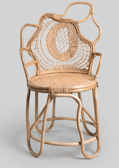 A unique armchair constructed from rattan. It features a woven seat and backrest with a distinctive circular pattern on the back. The frame is composed of bent rattan poles, creating an organic and sculptural silhouette with armrests extending from the sides and a curved top edge for the back support. The legs are also made from bent rattan poles, providing a stable base. — 3D model