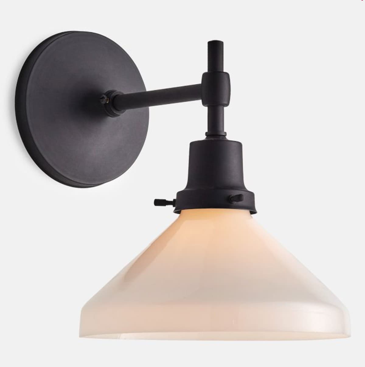 A contemporary wall sconce featuring a matte black finish on its metal components and a conical, opaque white glass shade. The fixture mounts to the wall with a circular backplate, from which a straight arm extends to support the downward-facing shade. — 3D model