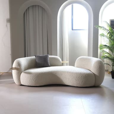 An off-white, intricately curved chaise lounge, upholstered in a textured boucle fabric. The design features an organic, asymmetric shape, with a higher backrest on one end and a lower, more open side on the other. Two small, round, bronze-toned integrated side tables or trays are set into the frame. A single small, patterned cushion rests on the chaise. — 3D model