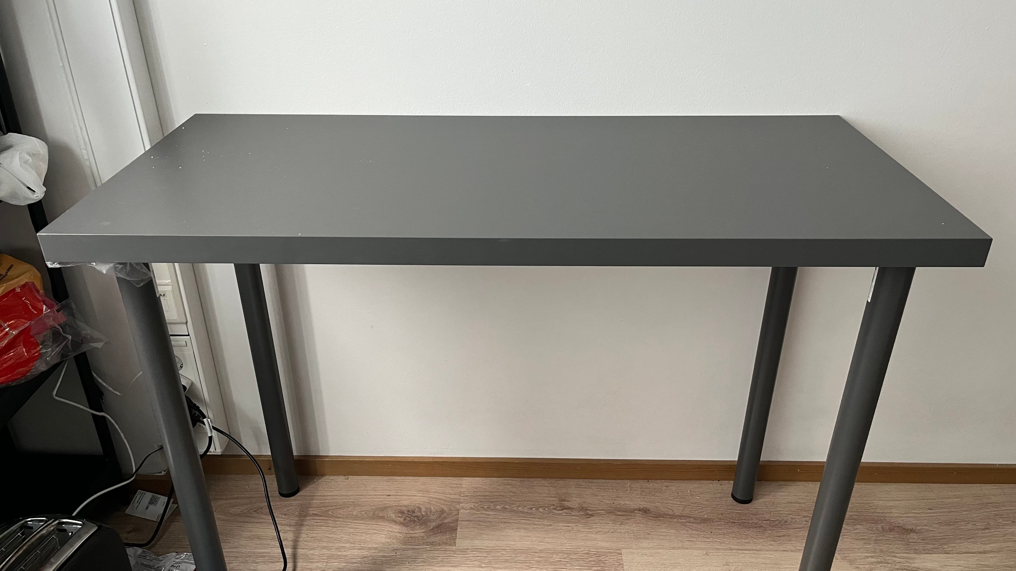A simple, minimalist rectangular table featuring a dark gray tabletop with rounded corners and four straight, cylindrical legs of the same dark gray color. The design is utilitarian and contemporary. — 3D model