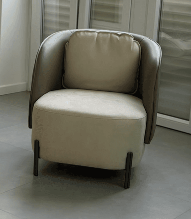 An upholstered tub-style accent chair featuring a two-tone design with a rounded back and integrated armrests. The outer shell is a darker brown, while the inner seat and separate back cushion are a lighter beige or tan. The chair is supported by four slender, angled black metal legs. — 3D model