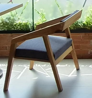 A modern wooden armchair featuring a light-toned wooden frame with a distinct geometric design. The chair includes integrated armrests and a solid backrest made from the same wood. The seat is fitted with a comfortable dark gray upholstered cushion, providing a contrast to the light wood. The overall aesthetic is clean and contemporary. — 3D model