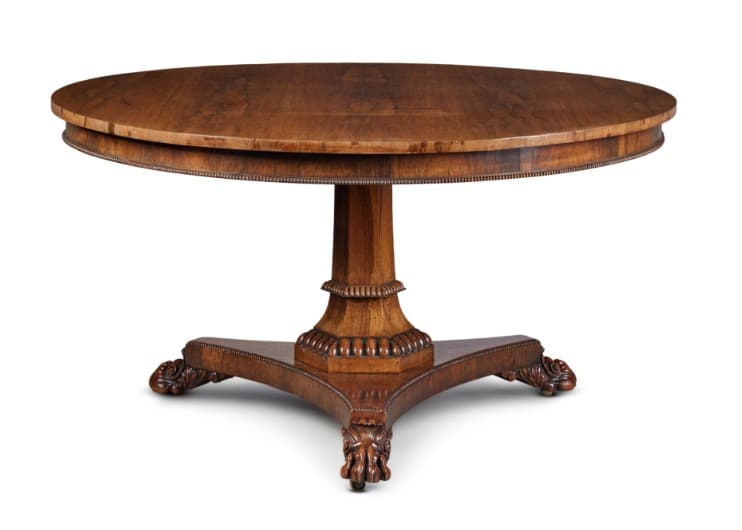 A round, wooden pedestal table with a rich, medium-brown finish. The tabletop features a finely reeded edge. It is supported by a central fluted column that rests on a tripartite base, with each splayed leg terminating in a carved paw foot. The base also features decorative carved detailing. — 3D model