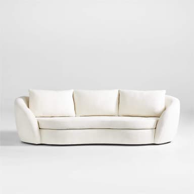 A modern three-seater sofa with a curved silhouette and plush upholstery. It features three loose back cushions and a continuous seat cushion. The arms are rounded and integrated into the overall curved design. The upholstery appears to be a textured fabric, possibly boucle or sherpa, in a light cream color. — 3D model