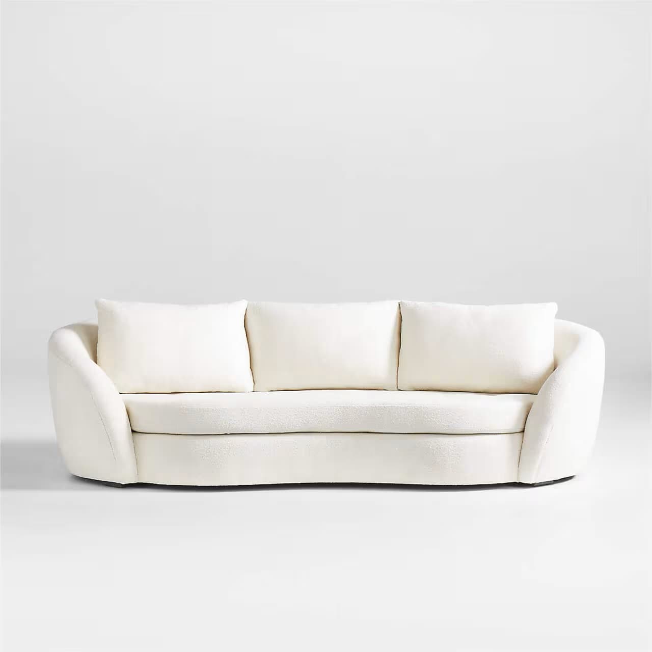 A modern three-seater sofa with a curved silhouette and plush upholstery. It features three loose back cushions and a continuous seat cushion. The arms are rounded and integrated into the overall curved design. The upholstery appears to be a textured fabric, possibly boucle or sherpa, in a light cream color. — 3D model