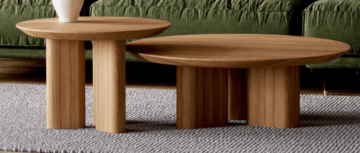 An oval-shaped coffee table with a natural wood finish. The table has a thick, rounded tabletop and two solid, block-like legs that are rounded at the edges and integrated into the underside of the tabletop. The wood grain is visible and runs longitudinally across the tabletop and vertically on the legs. — 3D model