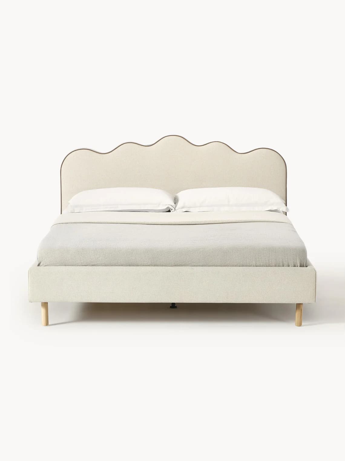 A cream-colored upholstered bed frame with a distinctive scalloped headboard. The entire frame, including the headboard, side rails, and footboard, is covered in a soft, textured fabric. The headboard features a wavy top edge with contrasting piping. The bed stands on four slender, light-toned tapered wooden legs. A white mattress and a light gray throw are visible on the bed. — 3D model