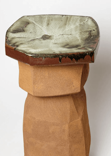 An octagonal pedestal table featuring a faceted, unglazed ceramic body in an earthy brown tone, topped with a smooth, glazed surface displaying a marbling pattern of white, brown, and green hues. The body has a roughly textured, almost Brutalist appearance, with its geometric angles creating a sculptural form. The base of the pedestal flares out slightly to form four integrated feet. The glazed top exhibits characteristic drips and variations where it meets the unglazed body. — 3D model
