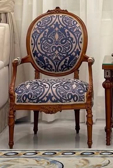 An ornate armchair featuring a carved wooden frame and upholstered in a blue and beige patterned fabric. The chair has an oval backrest, scroll-detailed arms, and cabriole legs. The wood frame exhibits intricate carvings, particularly on the crest rail, apron, and arm supports. — 3D model