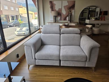 A modern two-seater sofa, upholstered in a light grey fabric, featuring two distinct seat cushions and two backrests with independently adjustable headrests. The sofa has gently curved, upholstered armrests and stands on slender, tapered metal legs. — 3D model