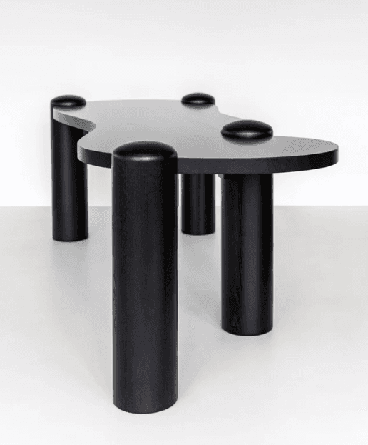 A black, abstractly shaped coffee table with a smooth, matte finish. It features a distinctively curved tabletop and four cylindrical legs. Each leg is topped with a rounded cap that complements the overall design. The piece has a modern, sculptural aesthetic. — 3D model