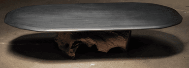 A low coffee table featuring an elongated oval top made of dark, matte material, possibly stone, supported by a unique and irregular base crafted from a natural wood root or stump. The design combines a sleek modern top with an organic, sculptural base. — 3D model