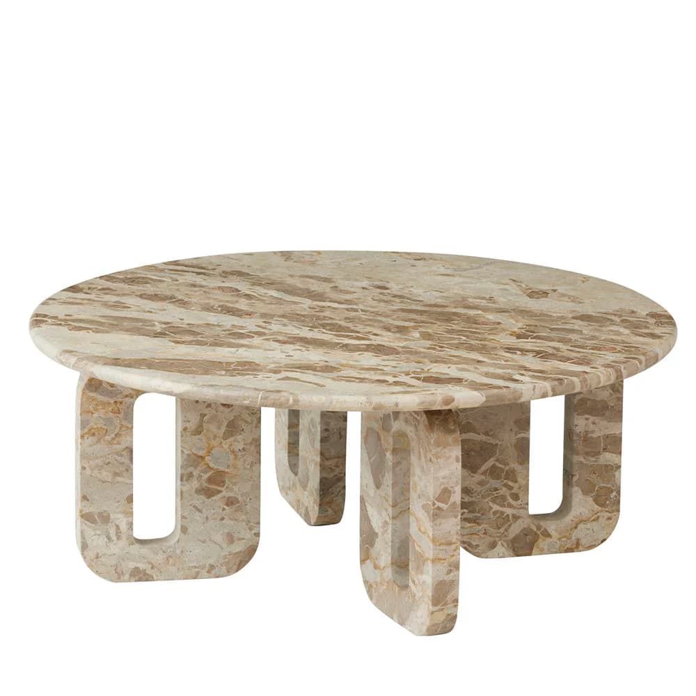 A low, round coffee table crafted entirely from light beige and brown marble, featuring a substantial circular top supported by four thick, sculptural legs. Each leg has a distinct rectangular cut-out, creating a monolithic yet visually interesting base with pronounced natural veining. — 3D model