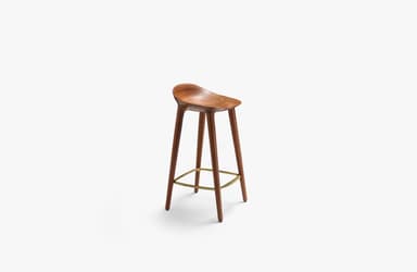 A modern bar stool crafted from dark brown wood, likely walnut, featuring a deeply sculpted saddle seat for ergonomic comfort. It stands on four slender, tapered legs that splay slightly outwards, connected by a triangular brass-toned metal footrest. The design is minimalist and contemporary, highlighting the natural beauty of the wood grain. — 3D model