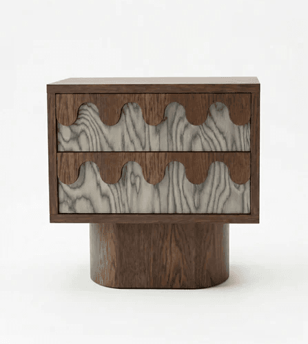 A contemporary nightstand featuring two drawers with a distinctive wave-like carved wooden facade. The main body and base are constructed from dark wood, while the drawer fronts exhibit a contrasting lighter wood with prominent grain patterns, also featuring the wave motif. The piece is supported by a solid, cylindrical wooden base. — 3D model