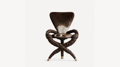 A unique and sculptural accent chair featuring an X-shaped base and armrests crafted from what appears to be dark, twisted wood or resin, giving a rope-like texture. The seat and backrest are upholstered in genuine cowhide, displaying a natural pattern of dark brown and white. The four legs of the base are each tipped with polished brass caps, adding a touch of elegance to its rustic yet modern design. — 3D model