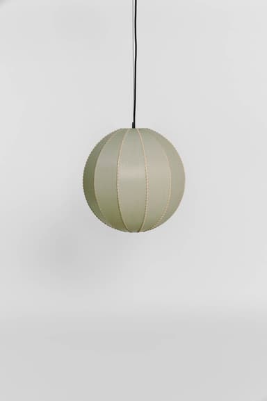 A spherical pendant light featuring a shade composed of multiple segmented panels, likely made from fabric or paper, in a soft sage green color. The segments are joined by visible stitching or seams, creating a distinct texture. The light is suspended from a black electrical cord. — 3D model