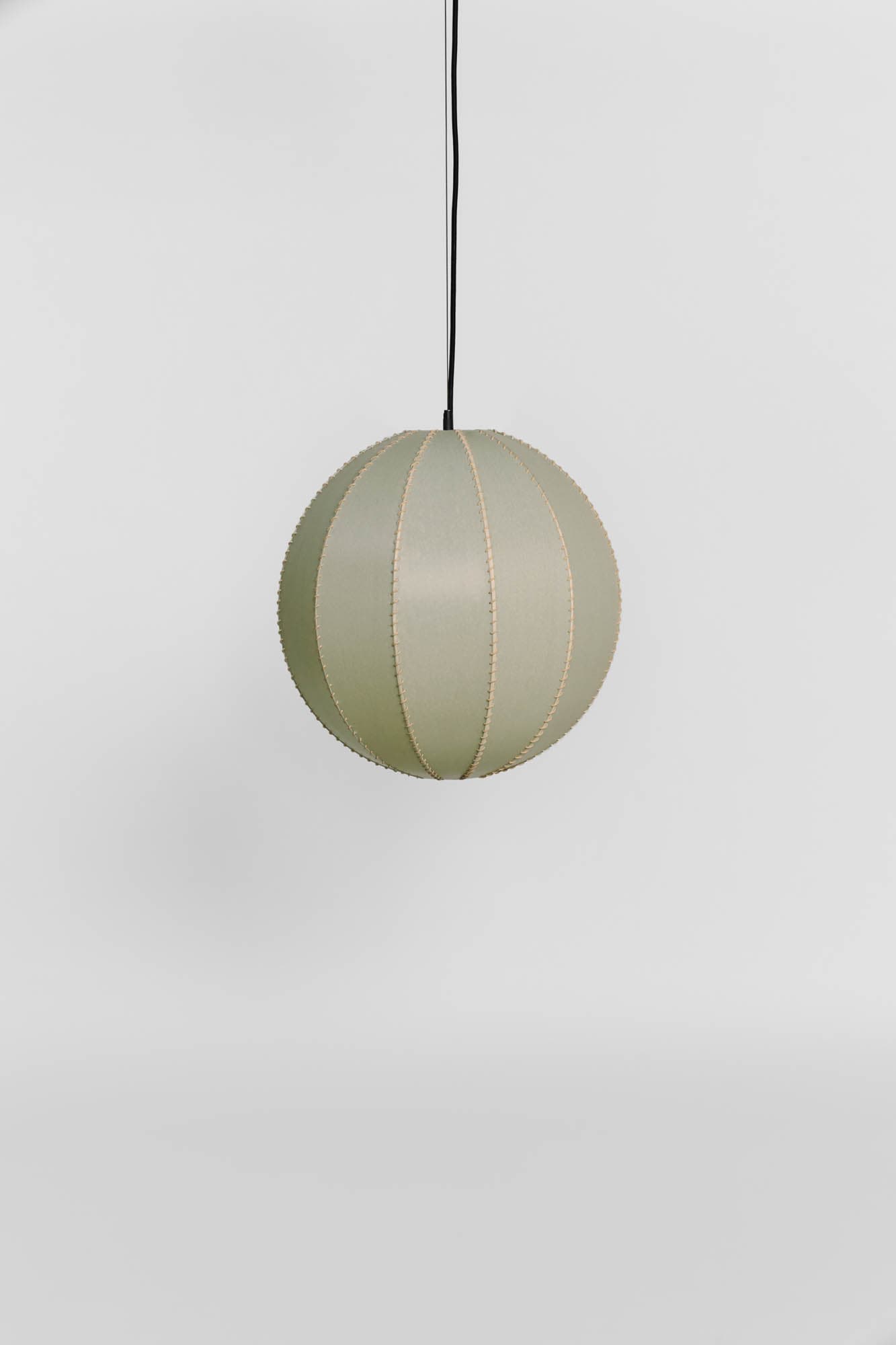 A spherical pendant light featuring a shade composed of multiple segmented panels, likely made from fabric or paper, in a soft sage green color. The segments are joined by visible stitching or seams, creating a distinct texture. The light is suspended from a black electrical cord. — 3D model