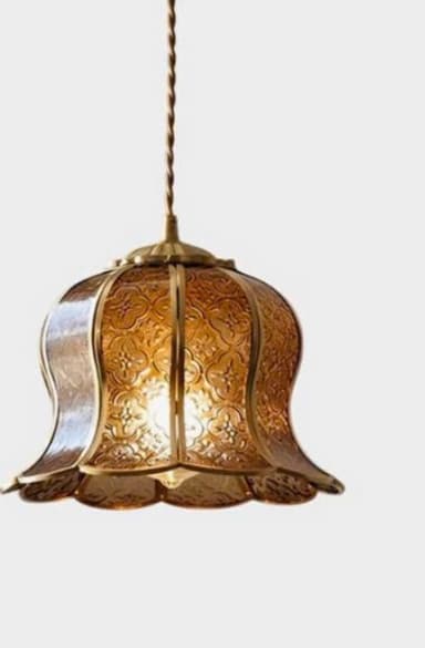 A vintage-style pendant light featuring a bell-shaped shade crafted from embossed amber glass panels set within a brass frame. The glass panels display an intricate floral or geometric pattern. The bottom edge of the shade is scalloped, and it is suspended by a twisted, braided cord. — 3D model