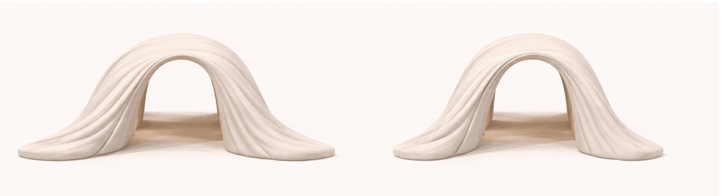 A beige, arch-shaped bench that appears to be made of a soft, pliable material. The bench has a smooth, matte finish with visible vertical pleats or folds that drape from the arch's apex to the base, creating a sense of soft drapery. The interior of the arch is hollow, suggesting it could be a functional bench with a unique, sculptural form. — 3D model