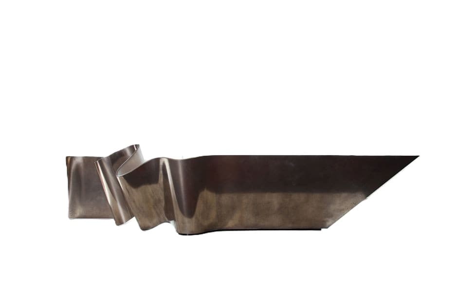 A sculptural coffee table with a fluid, undulating form resembling a ribbon or wave. The piece has a metallic sheen and appears to be constructed from a solid material, likely metal or a composite. Its design is avant-garde, with a sleek, continuous surface that undulates from a more upright form on the left to a flatter, elongated surface with a sharp, angled end on the right. The surface is smooth and reflective. — 3D model