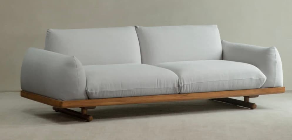 A two-seater sofa with a light grey upholstered body and a low-profile wooden base. The sofa features rounded armrests that extend slightly outwards and a minimalist design. The base is constructed from light-colored wood, possibly teak or oak, with subtle, angular legs. — 3D model