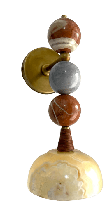 A wall-mounted lamp with a decorative design. The lamp features a circular brass mounting plate.  Extending from the plate is a vertical rod that supports three stacked spherical elements made of natural stone. The top sphere has brown and white banding. The middle sphere is grey. The bottom sphere mirrors the top one with brown and white banding. Below the spheres, a small, conical element wrapped in what appears to be twine or a similar material connects to a dome-shaped base, also made of natural stone with translucent yellow and white marbling. — 3D model