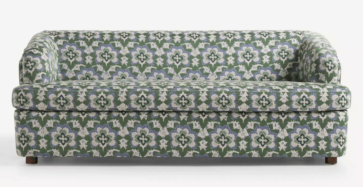 A three-seater sofa with a rounded armrest on the left side. The sofa is upholstered in a fabric with a repeating floral pattern in green, blue, and white. It has a solid base and short, wooden legs. — 3D model