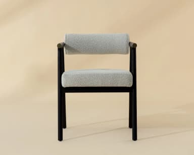 A contemporary armchair featuring a dark, possibly black-stained, wooden frame with clean lines. The seat and cylindrical backrest are upholstered in a light, textured fabric, resembling bouclé or a similar weave. The armrests are an extension of the frame, culminating in subtle brass-finished accents on the outer edges. The chair's design combines minimalist aesthetics with comfortable padding, suitable for various modern interiors. — 3D model