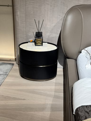 A circular end table with a dark wood finish on the exterior and a marble-patterned inlay on the top surface. The table features a two-tiered design, with the lower section appearing to be a drawer or cabinet. It is adorned with two books and a decorative diffuser. — 3D model