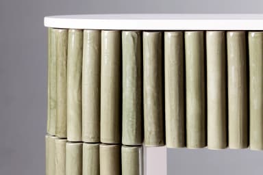 An elongated, narrow console table featuring a light pinkish-beige top and structural elements. The front and sides are extensively clad with vertical, muted green cylindrical elements, likely ceramic rods, creating a fluted or reeded texture. The base of the table follows the same pinkish-beige tone and features a subtle arched shape. — 3D model