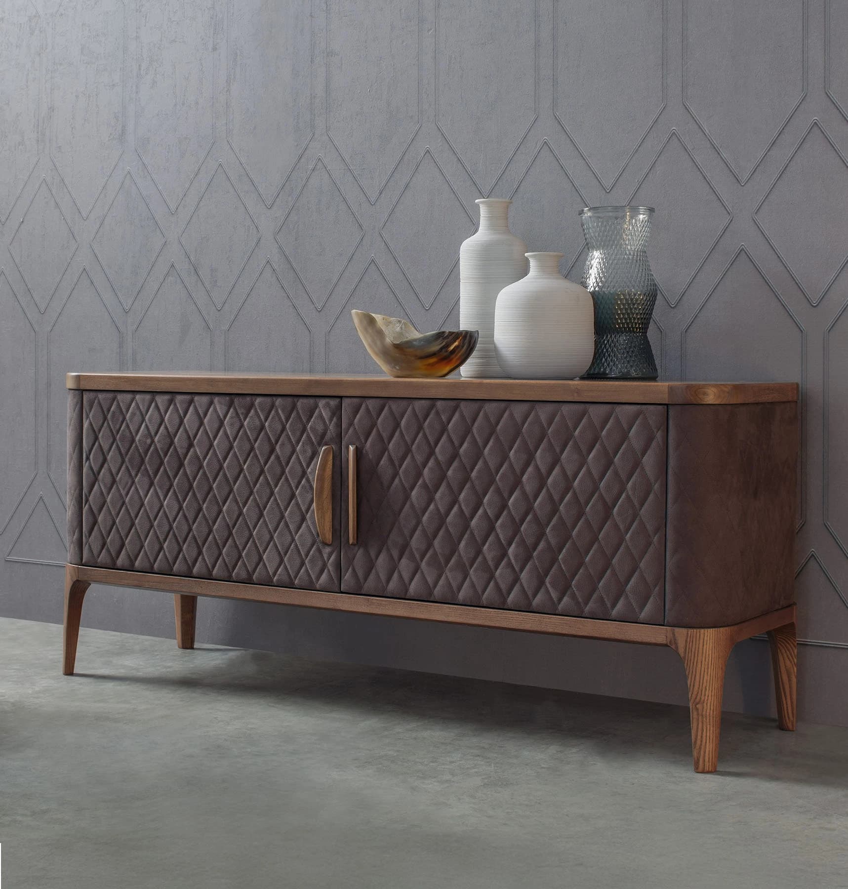 An elongated, low-profile media console featuring a rectangular wooden top with rounded corners. The body of the console is upholstered in a dark brown, diamond-quilted fabric, giving it a textural and sophisticated appearance. It includes two cabinet doors with integrated wooden pull handles, suggesting enclosed storage. The console is supported by four tapered wooden legs, adding to its modern aesthetic. The overall design combines natural wood elements with plush upholstery. — 3D model