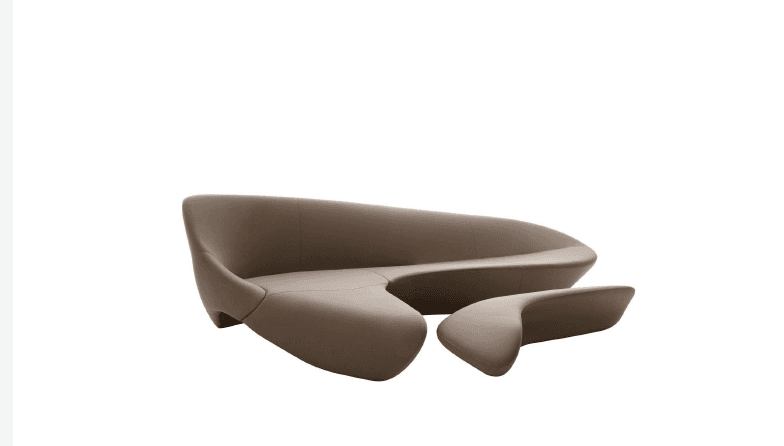 A fluid, organic-shaped sofa in a neutral taupe/mink brown color, featuring a continuous form that extends into an integrated chaise-like element. The design is armless and sculptural, with a low profile. — 3D model