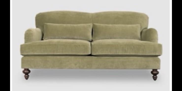 A traditional two-seater loveseat upholstered in a soft, sage green fabric, likely velvet or velour. It features rolled arms, a slightly flared backrest, and two loose back cushions. The base is supported by four dark, turned wooden feet. — 3D model