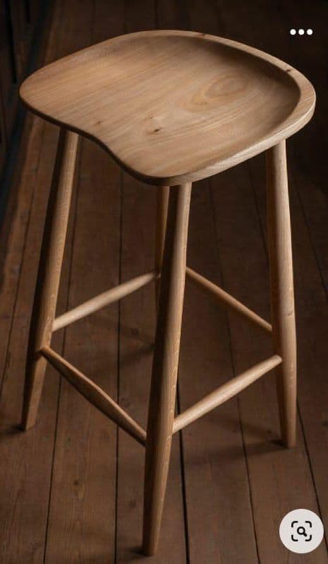 A tall, backless bar stool featuring a sculpted wooden seat and splayed, tapered legs connected by footrests. The stool is made from light-toned wood with a natural finish, showcasing minimalist Scandinavian-inspired design. — 3D model