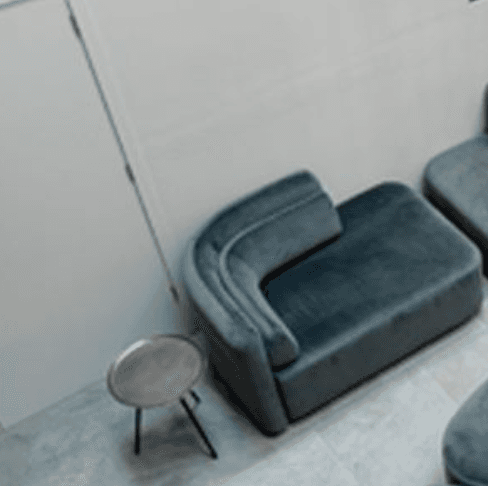 A corner armchair with a channel-tufted backrest and a plush seat cushion. The piece features a low profile and rounded edges, suggesting a modern or contemporary design aesthetic. It is upholstered in a soft-textured fabric. — 3D model