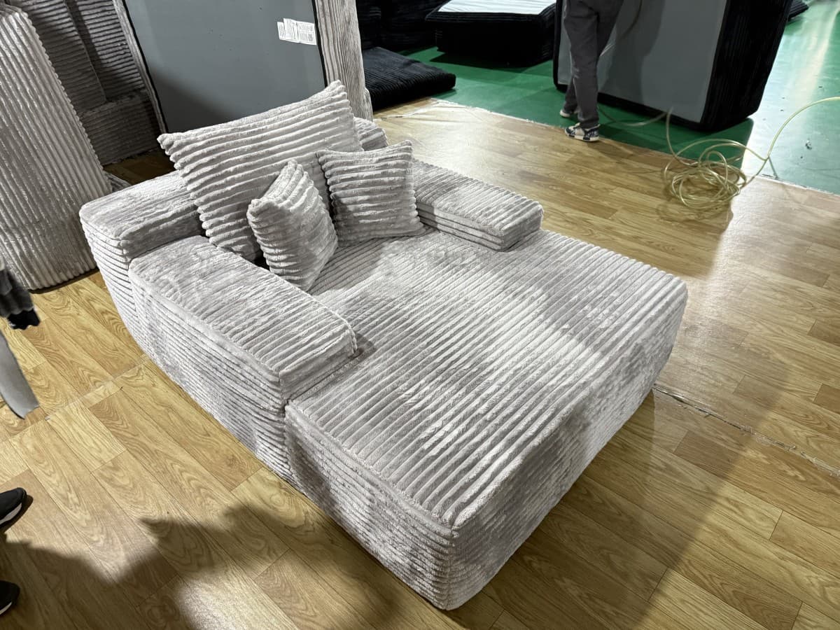A modular sectional sofa with a low profile and a contemporary design. The sofa features a ribbed corduroy upholstery and includes multiple throw pillows. The chaise lounge section is integrated into the overall structure. — 3D model