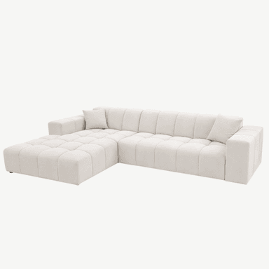 A contemporary sectional sofa with a tufted upholstery design. The sofa features a chaise lounge section extending from the main body. It is upholstered in a light cream-colored fabric with a soft texture. The design incorporates horizontal tufting on the seat and back cushions, creating a grid-like pattern. Two square throw pillows, matching the sofa's upholstery, are placed on the sofa. The sofa sits on low-profile, dark-colored feet. — 3D model