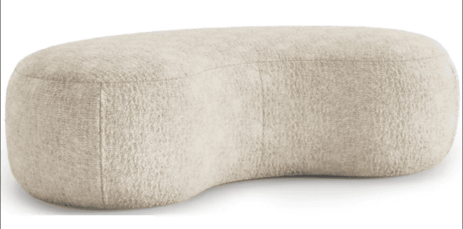 A low-profile, rounded ottoman with a unique, kidney-bean-like shape. It features a textured fabric upholstery and appears to be softly padded. The stitching is visible along the edges, indicating its construction. — 3D model