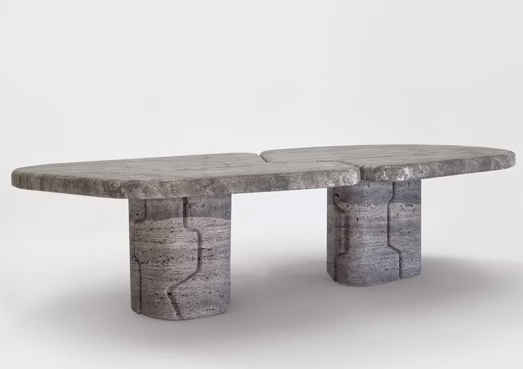 A contemporary coffee table constructed from gray travertine, featuring a distinctive split-top design. The tabletop consists of two rounded, oblong sections that meet in the middle with a narrow gap. Each section is supported by a robust, cylindrical pedestal base. The travertine exhibits a natural, textured, porous surface and varied gray tones. — 3D model
